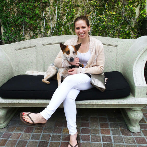 A female dog owner sitting on a concrete bench with a cattle dog.