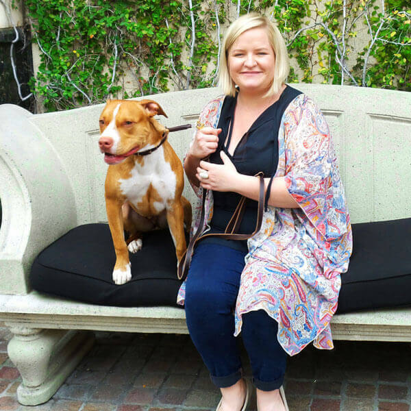 A female owner sitting on a concrete bench with a pit bull.
